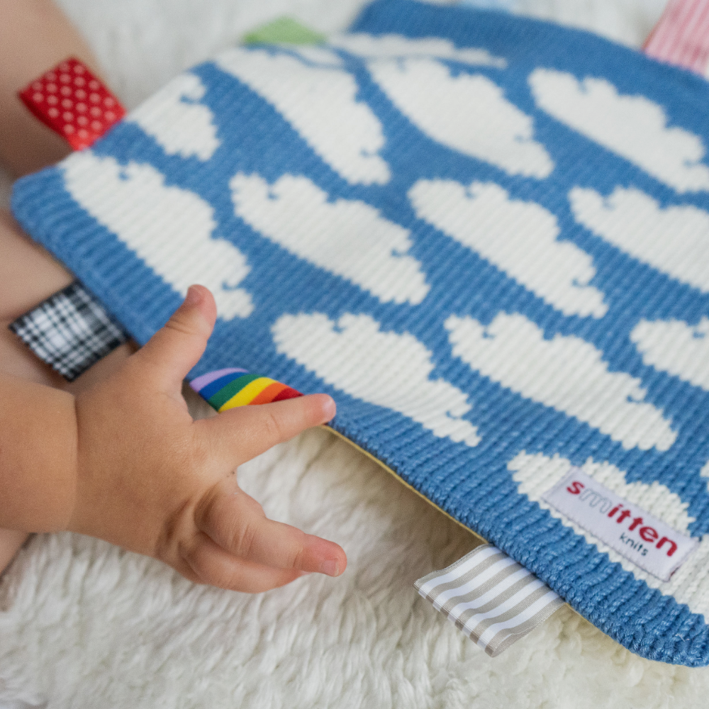 baby playing with a knitted comforter white clouds on a blue sky smitten knits 